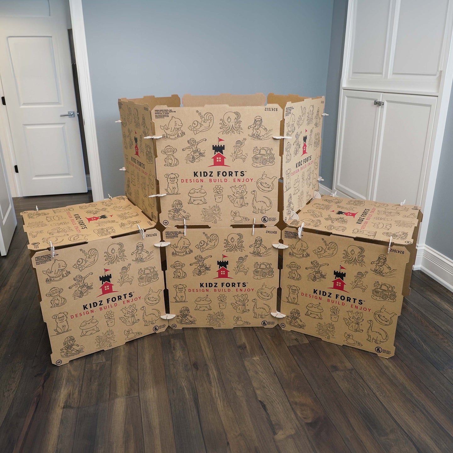 A photo of a Kidz Forts Hobie Kit children's play fort. The kit is made from cardboard and is printed with red and black ink. The fort has cartoon characters printed on it.