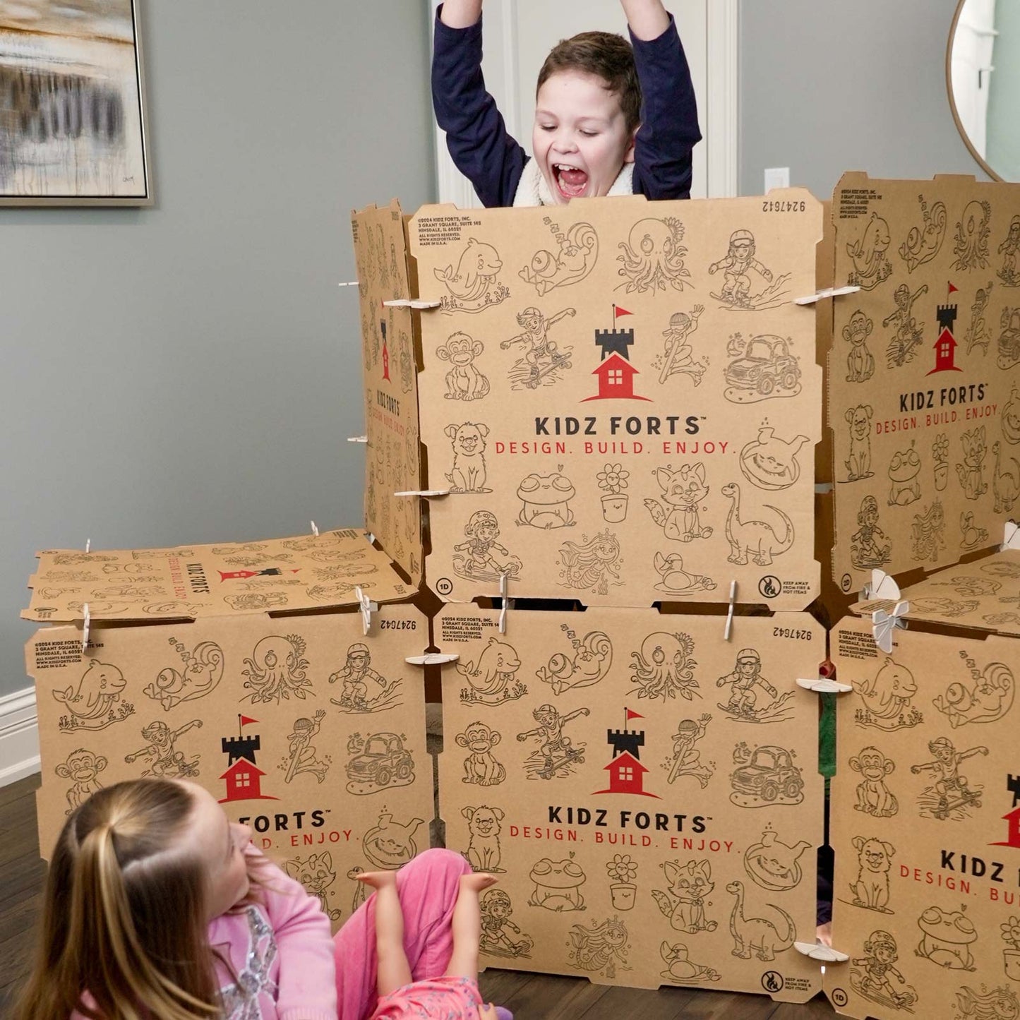 Image of a boy popping up from behind a Kidz Forts Hobie kit play fort, scaring a girl wearing a pink shirt and pink pants.