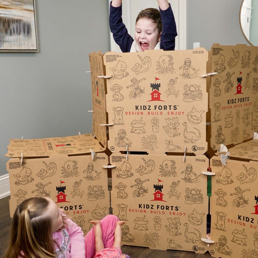 Image of a boy popping up from behind a Kidz Forts Hobie kit play fort, scaring a girl wearing a pink shirt and pink pants.