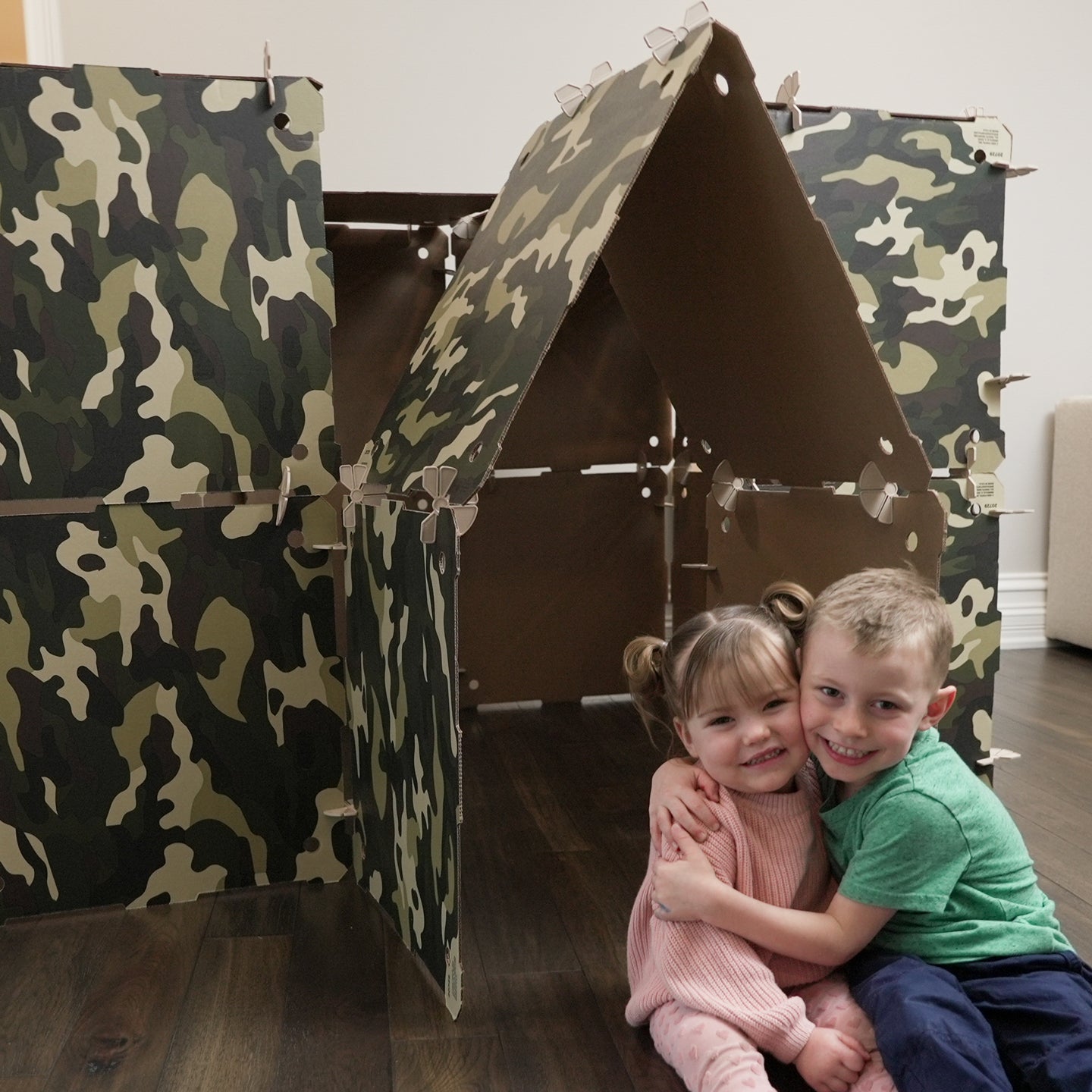 A boy and girl hugging and smiling while posing in front of a Kidz Forts Commando kit play fort.