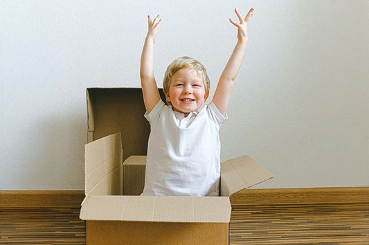 Boy in a cardboard box holding his arms in the air and smiling.