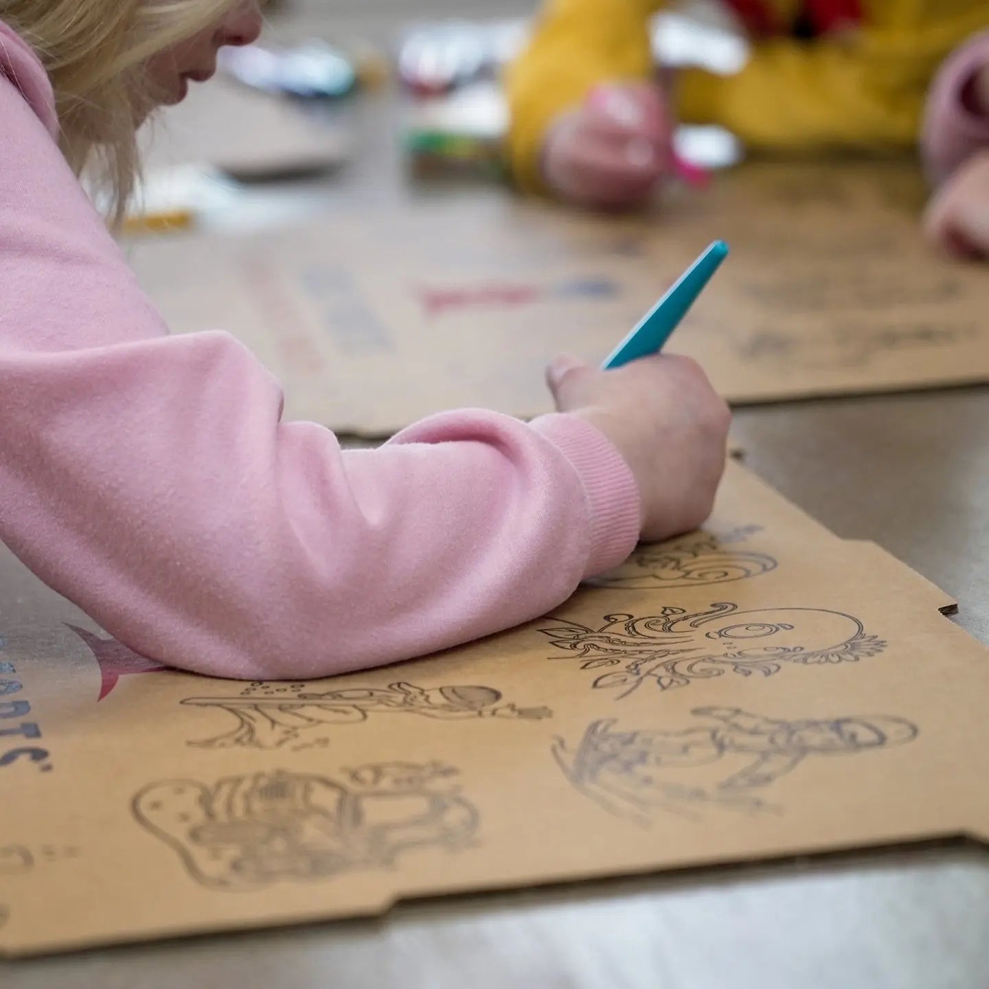 Kidz Forts Hobie Kit: Child in pink sweatshirt drawing on cardboard fort pieces with blue marker.