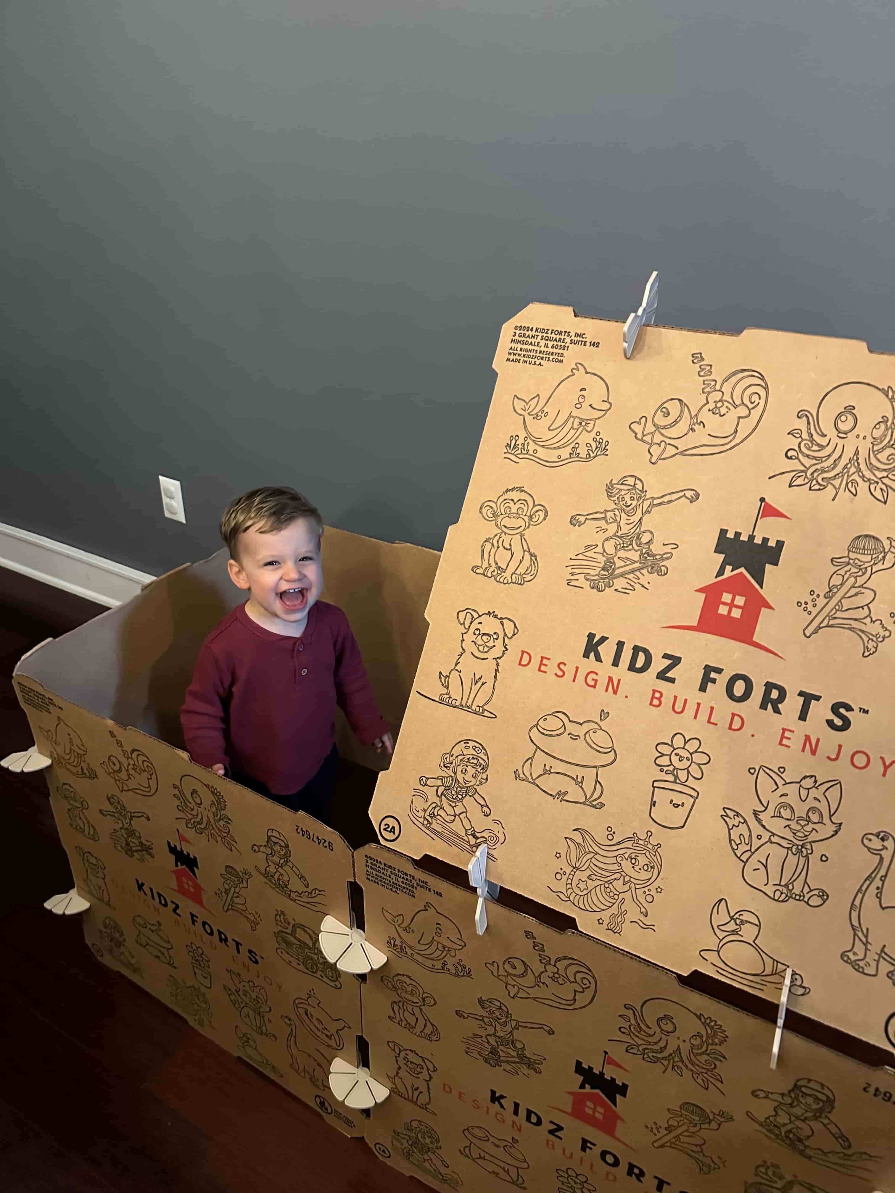 Little boy playing inside a cardboard  play fort building kit by Kidz Forts.