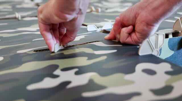 A set of hands connecting two kids play fort panels together using a plastic connector.  Fort has camouflage printing.