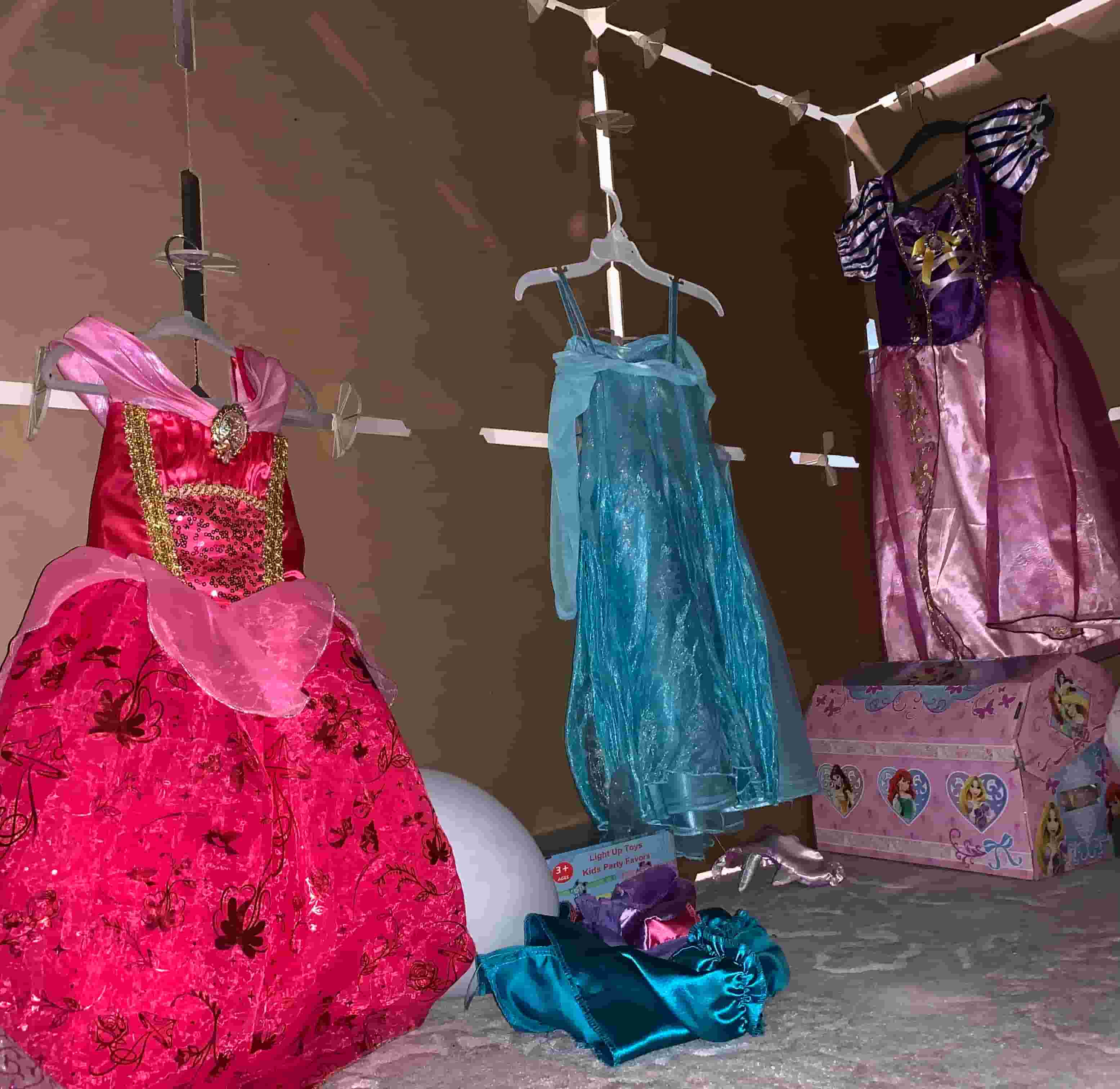 Children's dresses hanging on a rack with a box of toys in the background.