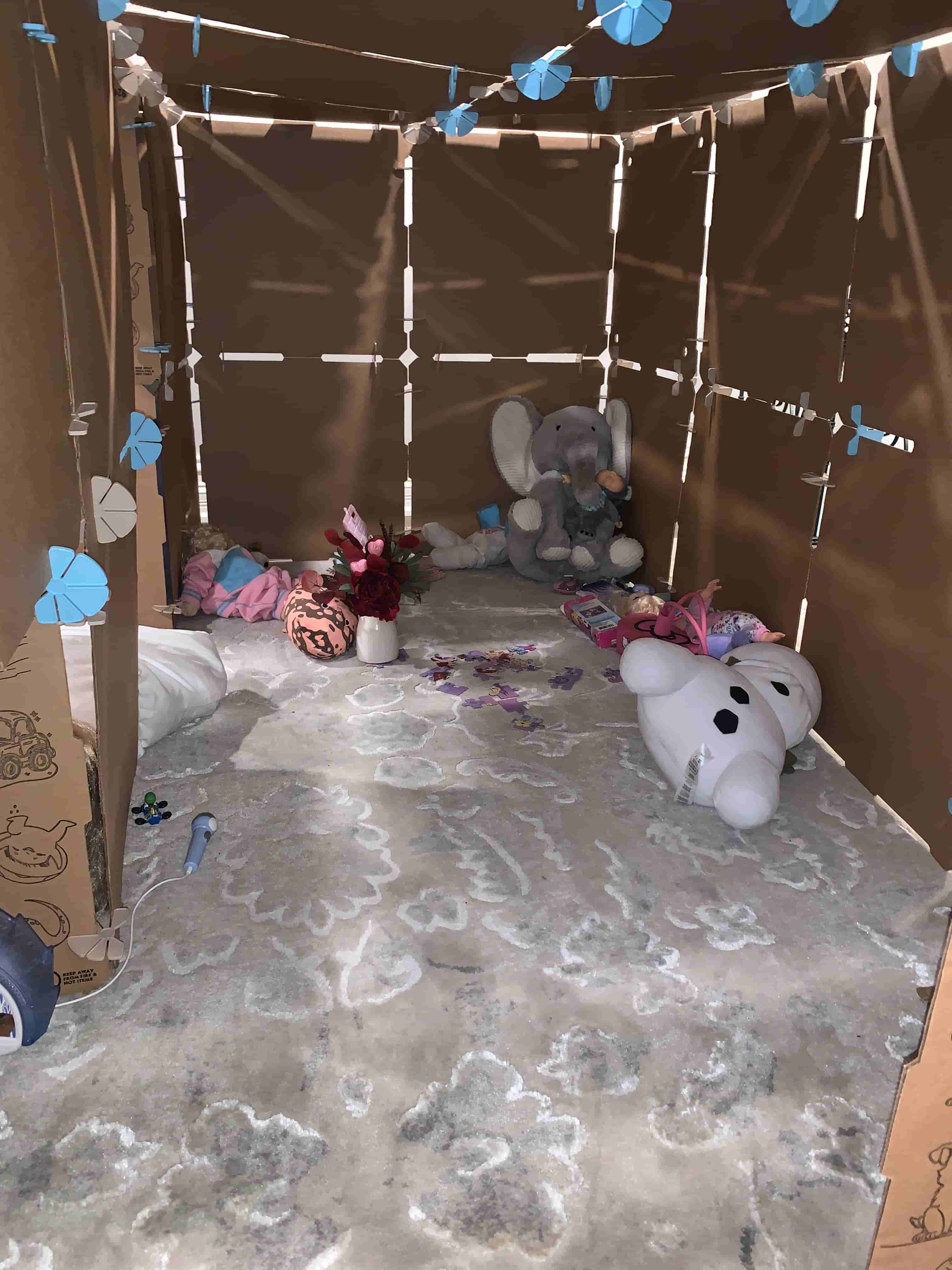 Children's toys on an area rug inside a cardboard play fort buidlng kit by Kidz Forts.