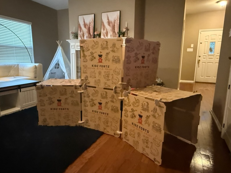 Cardboard playhouse set up in a living room with furniture and decor.